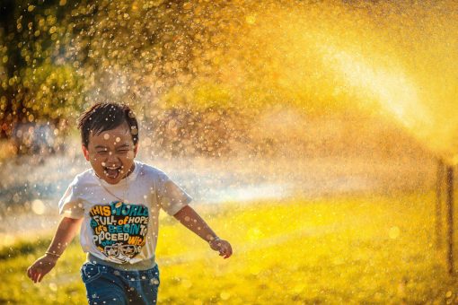 boy running through sprinklers